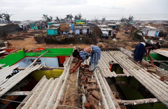 Women repair the roof of their houses at the cyclone-hit Nalianuagaon village in Ganjam district, Orissa.