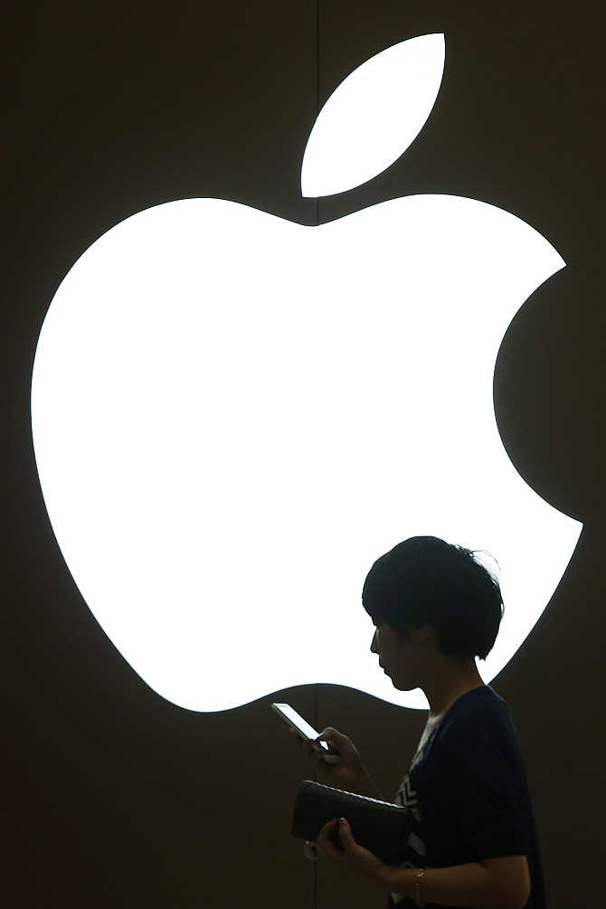 A woman looks at the screen of her mobile phone in front of an Apple logo outside its store in downtown Shanghai, China.