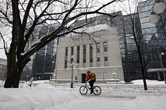 A cyclist passes the Bank of Canada building through a snow covered sidewalk in Ottawa.
