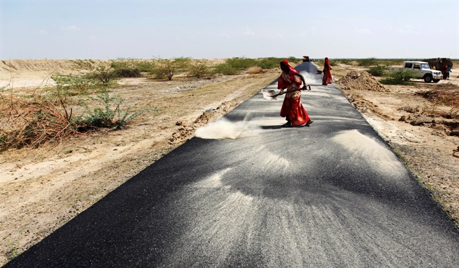 Women labourers throw dust on a road tarmac under construction at Bharadva village, Gujarat.