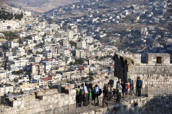 Arab neighbourhoods in East Jerusalem are seen in the background as tourists walk atop a wall surrounding Jerusalem's Old City.