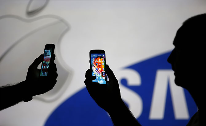 Men are silhouetted against a video screen with Apple and Samsung logos.