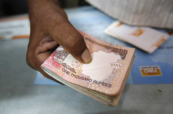 A customer hands a bundle of rupee currency notes to a teller at a financial institution in Mumbai.