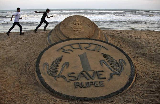 Boys run near a sand sculpture of the Rupee created by artist Sudarshan Pattnaik at golden sea beach in Puri, Orissa.