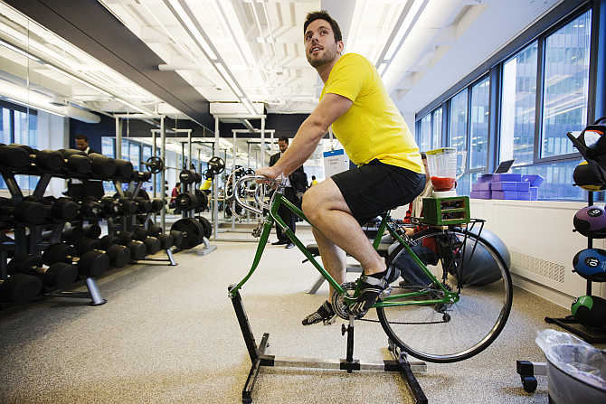 An employee demonstrates the use of an exercise cycle, that powers a blender making a fruit smoothie, inside the gym at the Google office in Toronto, Canada.