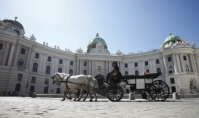 A Fiaker horse carriage passes Hofburg palace during a sunny spring day in Vienna, Austria.
