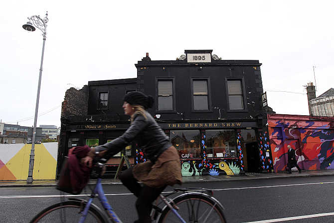 A woman cycles past the Coffee To Get Her restaurant near Dublin city centre which becomes a bar and club in the evenings, Ireland.