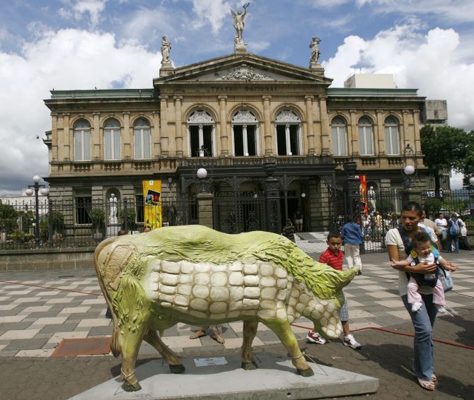 People walk past a cow sculpture on display in front of the National Theater during a Cow Parade art festival in San Jose.