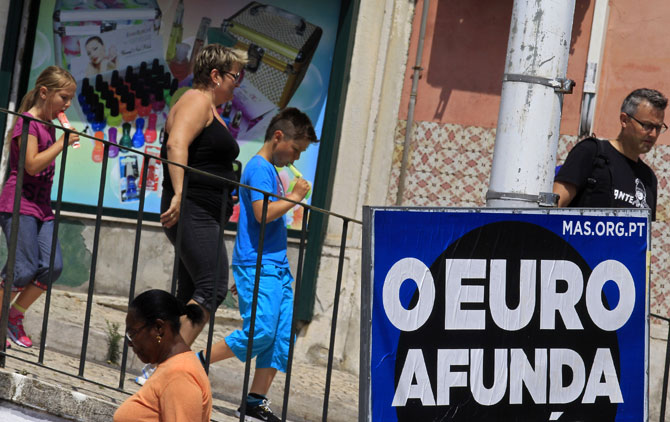 People walk past a political billboard with the phrase The euro sinks.