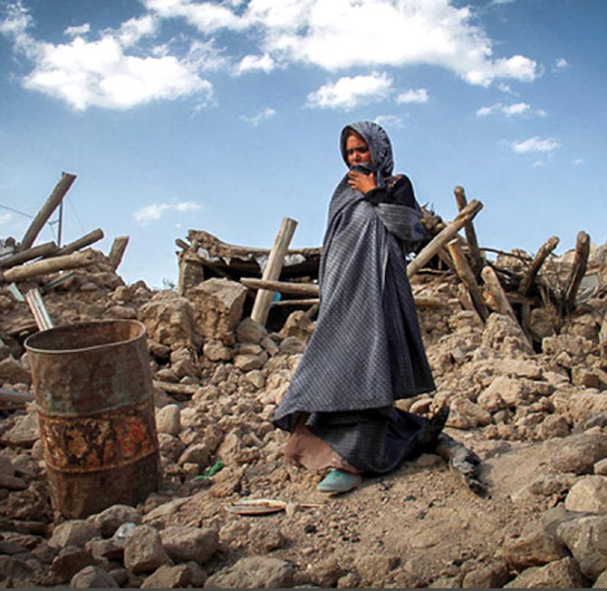 An earthquake victim stands near damaged houses.
