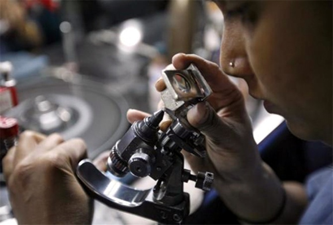 An employee checks the shape of a diamond through a magnifying glass, inside the polishing department of a diamond processing unit at Surat.