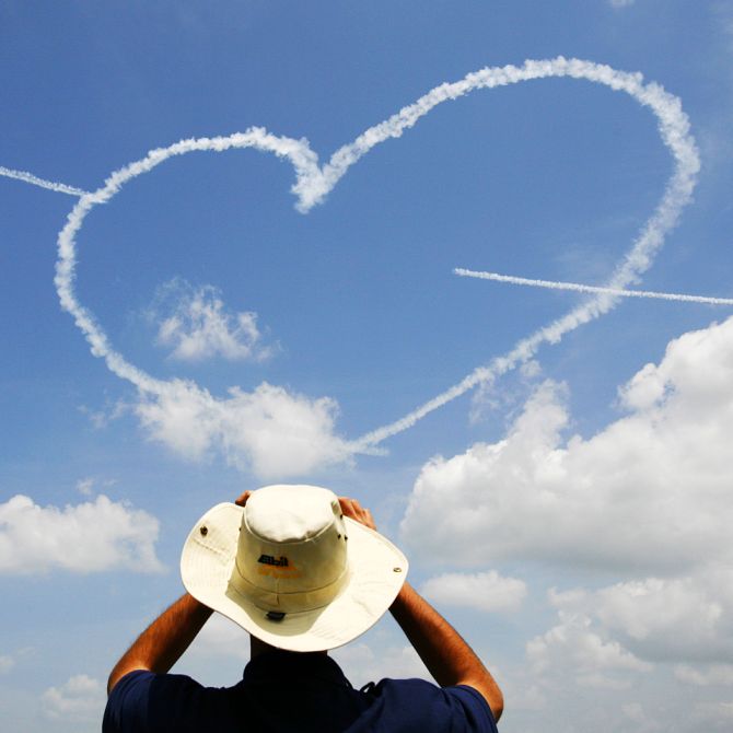 A man takes a photo as members of the Republic of Singapore Air Force (RSAF) Black Knights aerobatic team form a heart shape using smoke trails during a performance at the Singapore Air Show in Singapore.