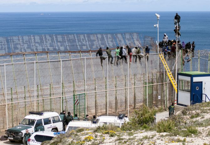 African migrants sit on top of a border fence covered in razor wire between Morocco and Spain's north African enclave of Melilla during their latest attempt to cross into Spanish territory.