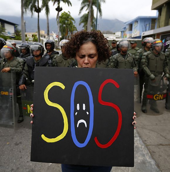 A demonstrator holds a placard as she stands in front of national guards during a protest near Cuba's embassy in Caracas.
