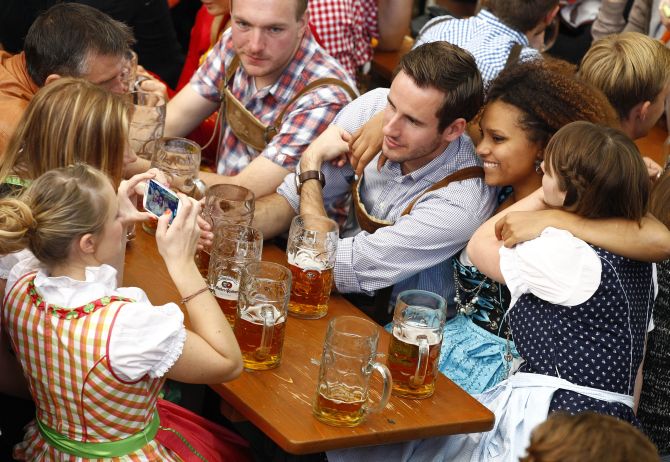 A young woman in a traditional Bavarian dirndl uses a mobile phone to take a picture of her friends.