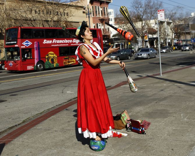 Street performer Carla Milugo juggles on a sidewalk while balancing on a ball in San Francisco.