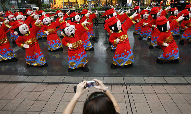 A bystander takes pictures as performers dressed as Chinese Fortune Gods dance in Singapore.