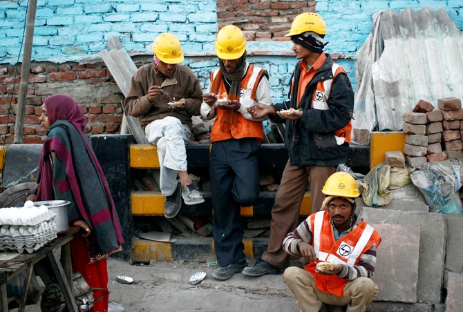 Labourers eat during a break from their work at the site of a commercial building under construction in Noida.