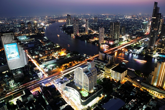 Cars and trains move on Taksin bridge over Chao Phraya river in central Bangkok at sunset.