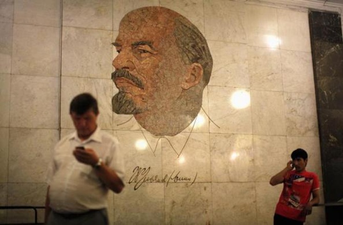 Men use their mobile phones as they stand in front of a mosaic depicting former Soviet leader Vladimir Lenin at Biblioteka Imeni Lenina metro station in Moscow.