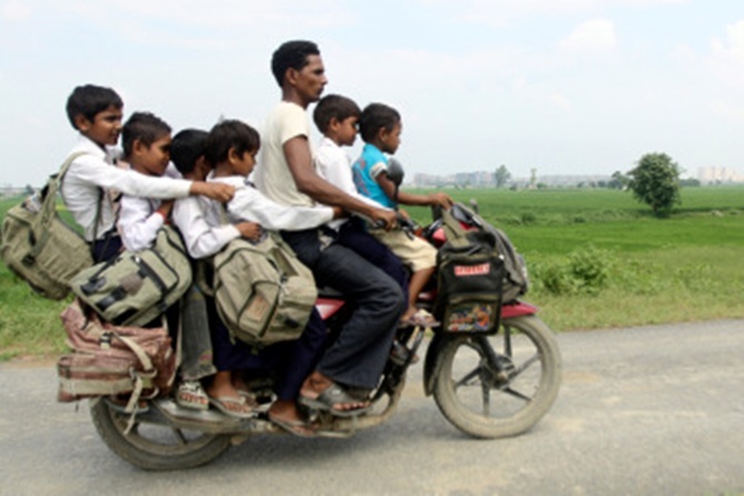 A man rides a motorcycle carrying six children on their way back home from school at Greater Noida.