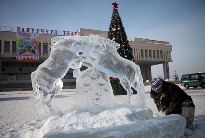 A worker works on an ice sculpture of horses in front of a giant Christmas tree to celebrate Christmas at the Youth Theatre in Darkhan city, Mongolia.