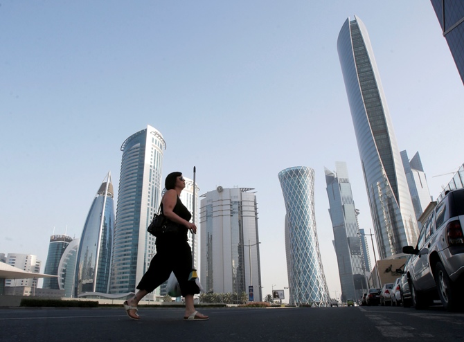 A woman crosses Al Wahda street hosting the Navigation Tower, headquarters of Qatargas (R), and Rasgas tower (2nd R) in Doha.