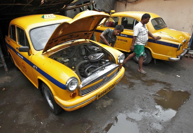 A mechanic repairs a yellow ambassador taxi at a workshop in Kolkata.