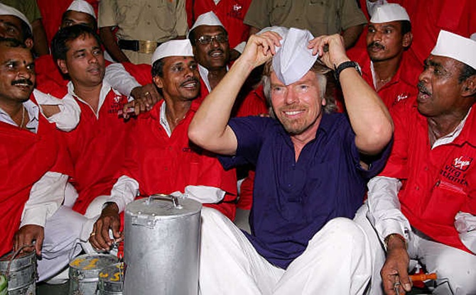 Richard Branson wears a cap as he sits amid lunch couriers, known as 'dabbawallas', at a railway station in Mumbai.