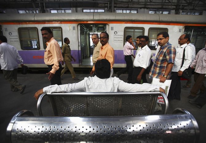 Commuters pass by as a man sits and waits for a train at Church Gate railway station in Mumbai.