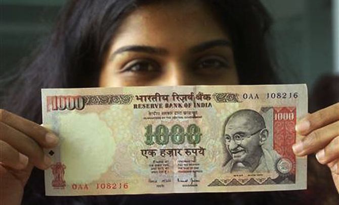 A girl displays a 1000 rupee note.