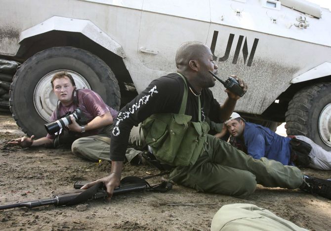 Reuters Congo correspondent David Lewis (L) takes cover behind a U.N. armoured car during machine gun and mortar fire in Kinshasa.