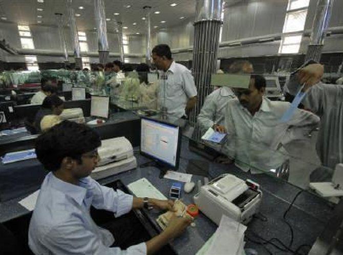 A cashier (L) counts currency notes as customers wait inside a bank in Hyderabad March 22, 2010. 