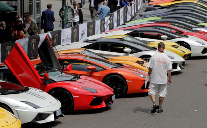 A man walks past Lamborghini sports cars parked at a car paddock during an event to mark the 50th anniversary of the carmaker in downtown Milan.