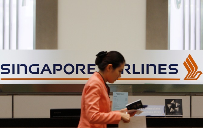 A staff member walks by a Singapore Airlines (SIA) logo at a ticketing counter.