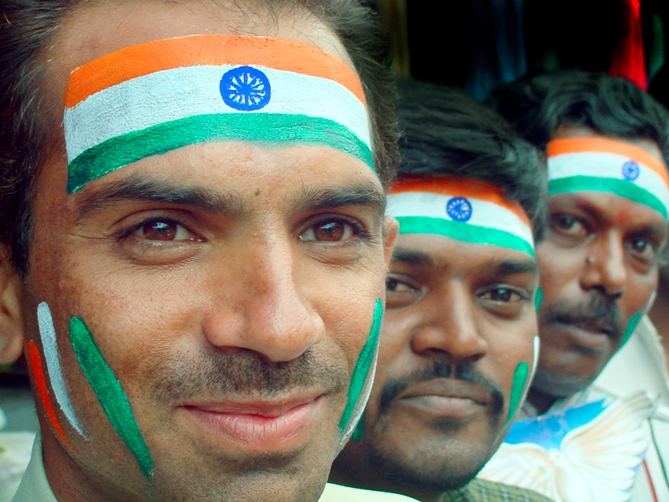 Indian men with their faces painted in the Indian tricolour.