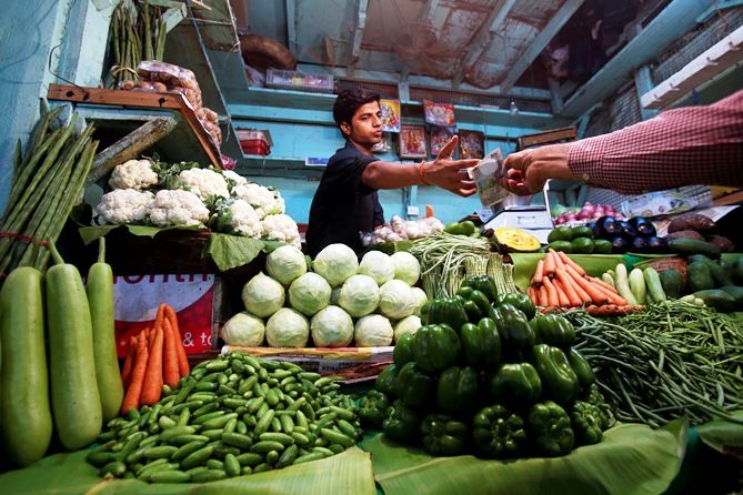A vendor accepts money from a customer at his vegetable stall at a wholesale fruit and vegetable market in Mumbai.