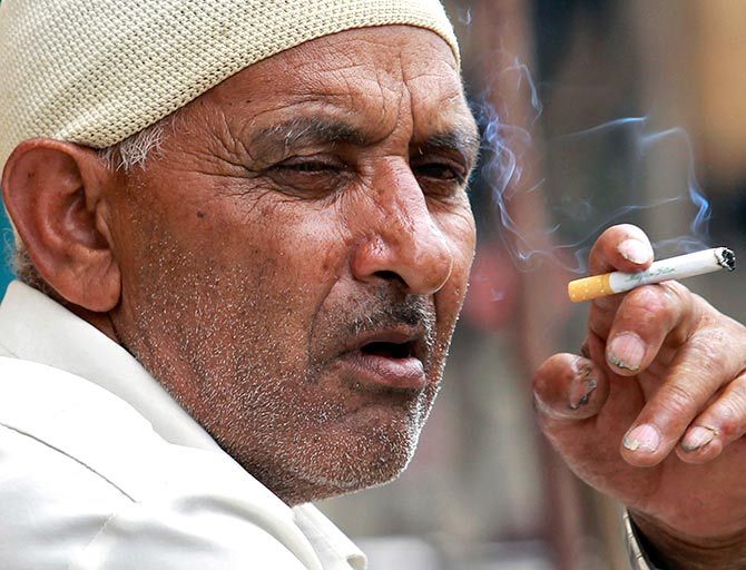 Image: A man smokes a cigarette as he sits on a pavement along a road in Srinagar. 