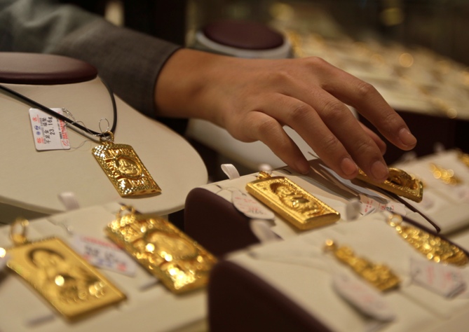 A sales assistant puts back a gold Buddha-shaped pendant after showing to a customer at Caibai Ornaments store in Beijing. Photograph: Petar Kujundzic/Reuters