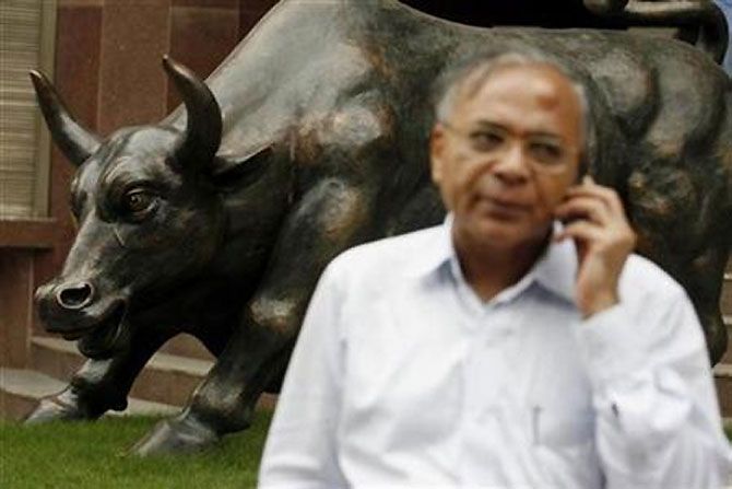 A man speaks on the phone in front of the bronz Bull statue at the Bombay Stock Exchange