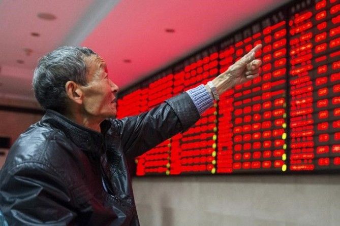 An investor points to an electronic board showing stock information as he speaks to another investor, at a brokerage house in Nanjing, Jiangsu province, China, November 19, 2015.