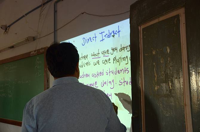 A school teacher makes use of  projector-aided teaching tool to explain grammar concepts to his students at the secondary school in Akodara