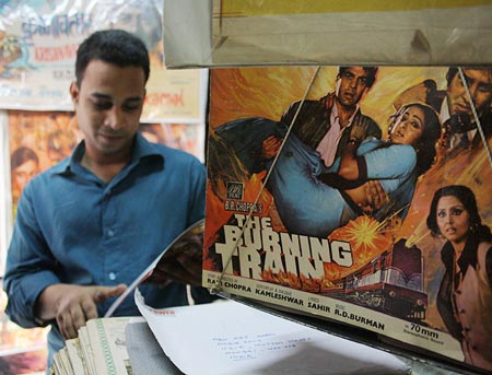 Haji Abu stands next to the poster of The Burning Train