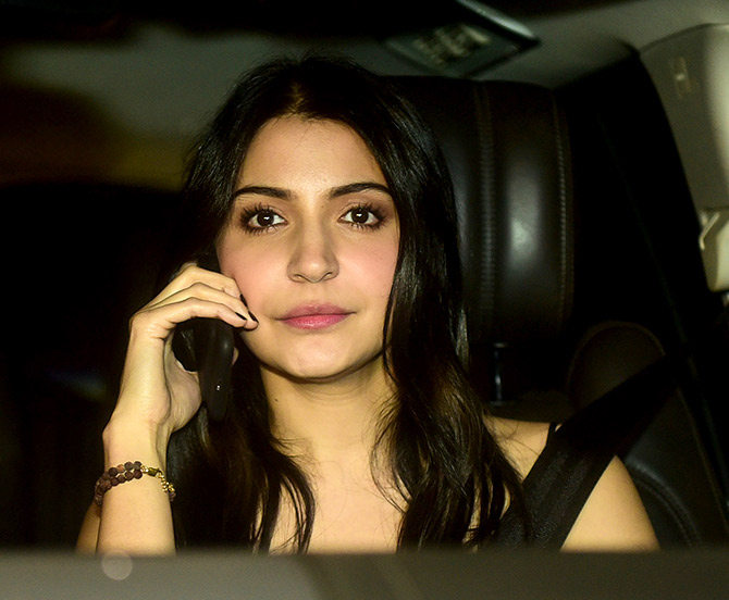 Anuska Sharma chats on her phone, seat belt firmly in place.