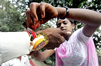 A woman threads rakhi on the wrist of her brother