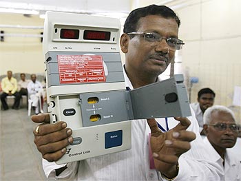 An officer holds a mock electronic voting machine as he explains the counting procedure to staff