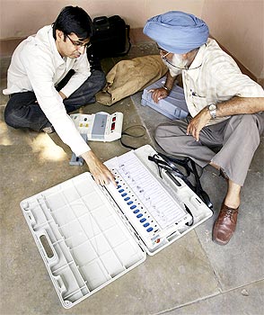 Polling officers check an EVM at a distribution centre