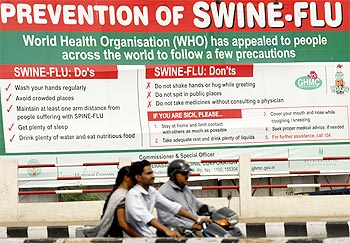 People ride past a billboard carrying messages on prevention of the Influenza A (H1N1) virus in Hyderabad