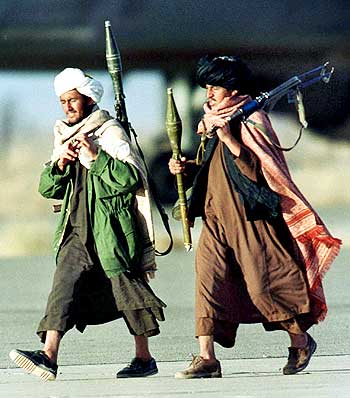 Taliban militiamen carrying machine guns and rocket-propelled grenades pass near the hijacked Indian Airlines Airbus A300