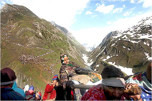 Porters carry an old woman to the shrine even as thousands follow behind